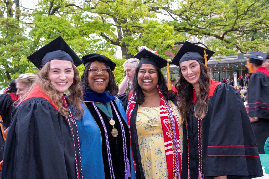 Graduates in cap and gown pose with Dean Linda Scott.