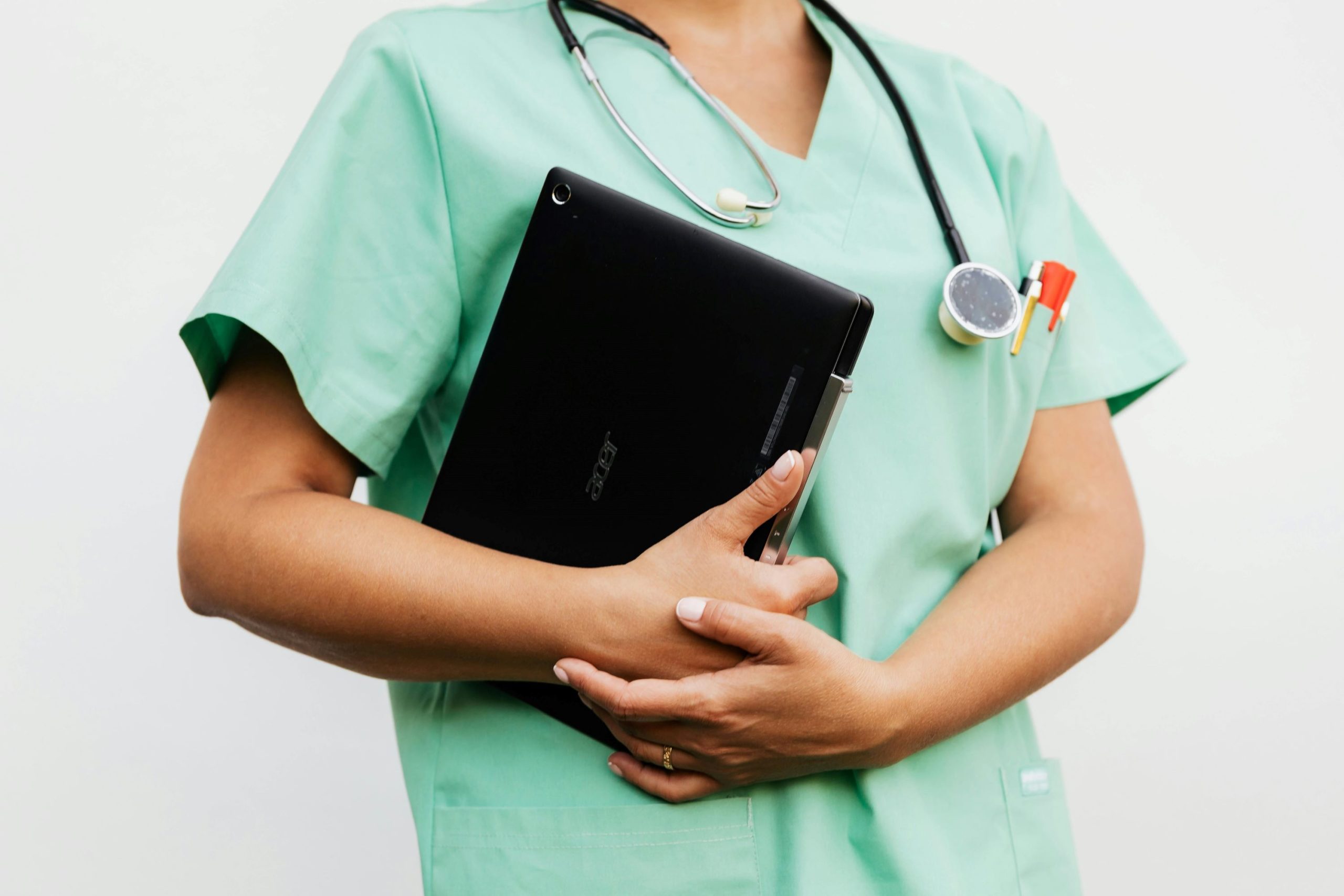 A nurse in blue scrubs holds a laptop.