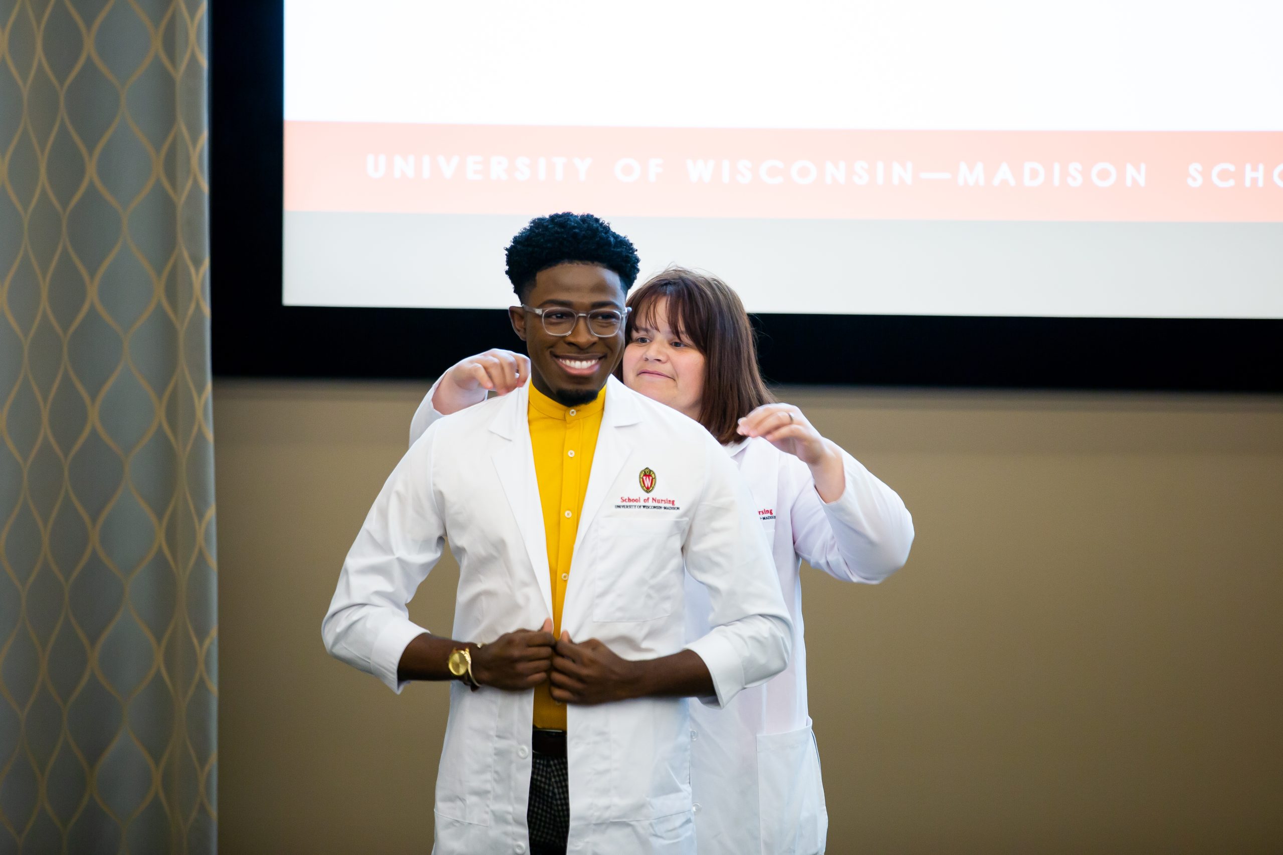 Elisha Smith ’14, DNP’21, gets some assistance as he puts on his white coat at the DNP recognition ceremony.