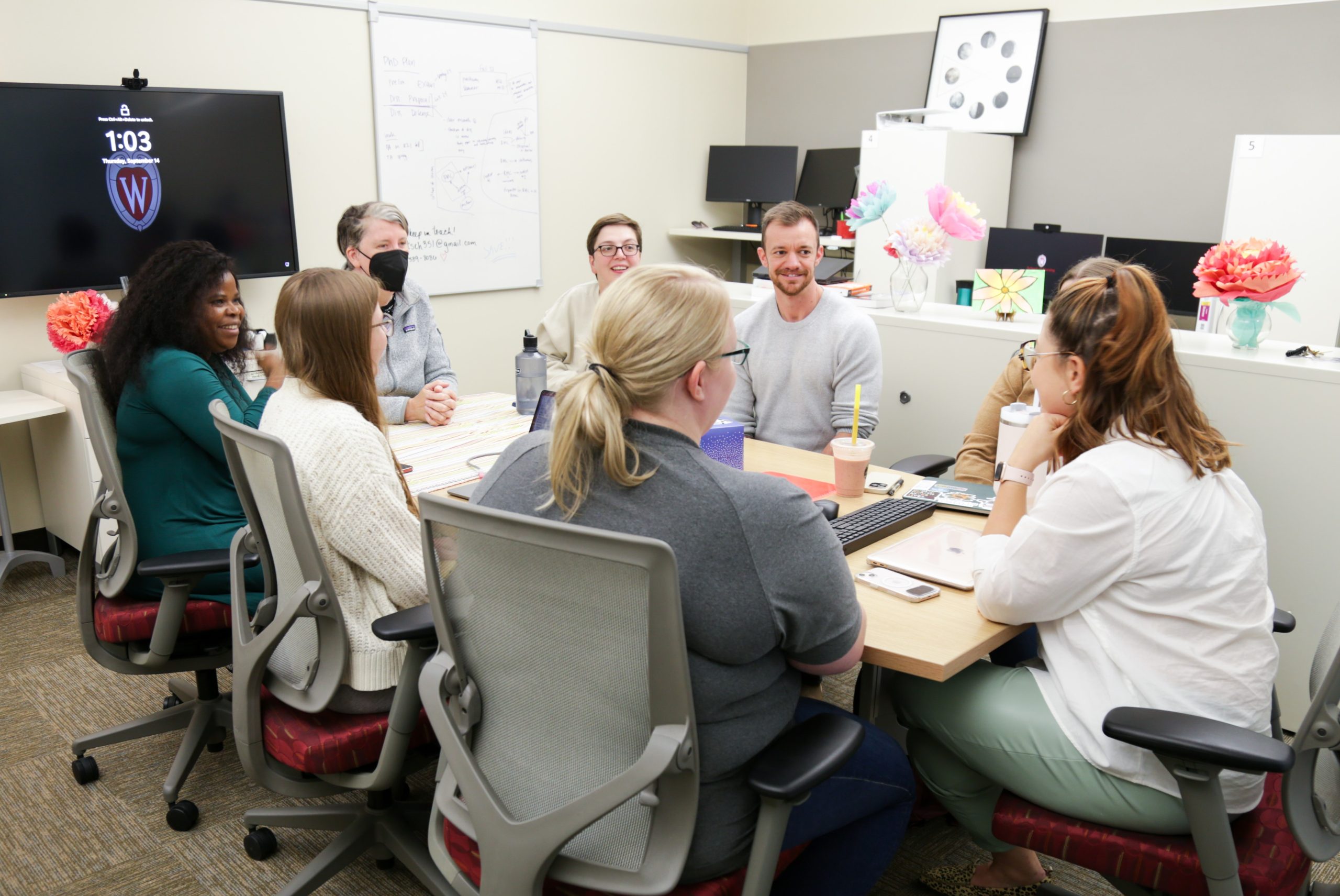 PhD faculty and students sit around a table in the PhD research workspace.