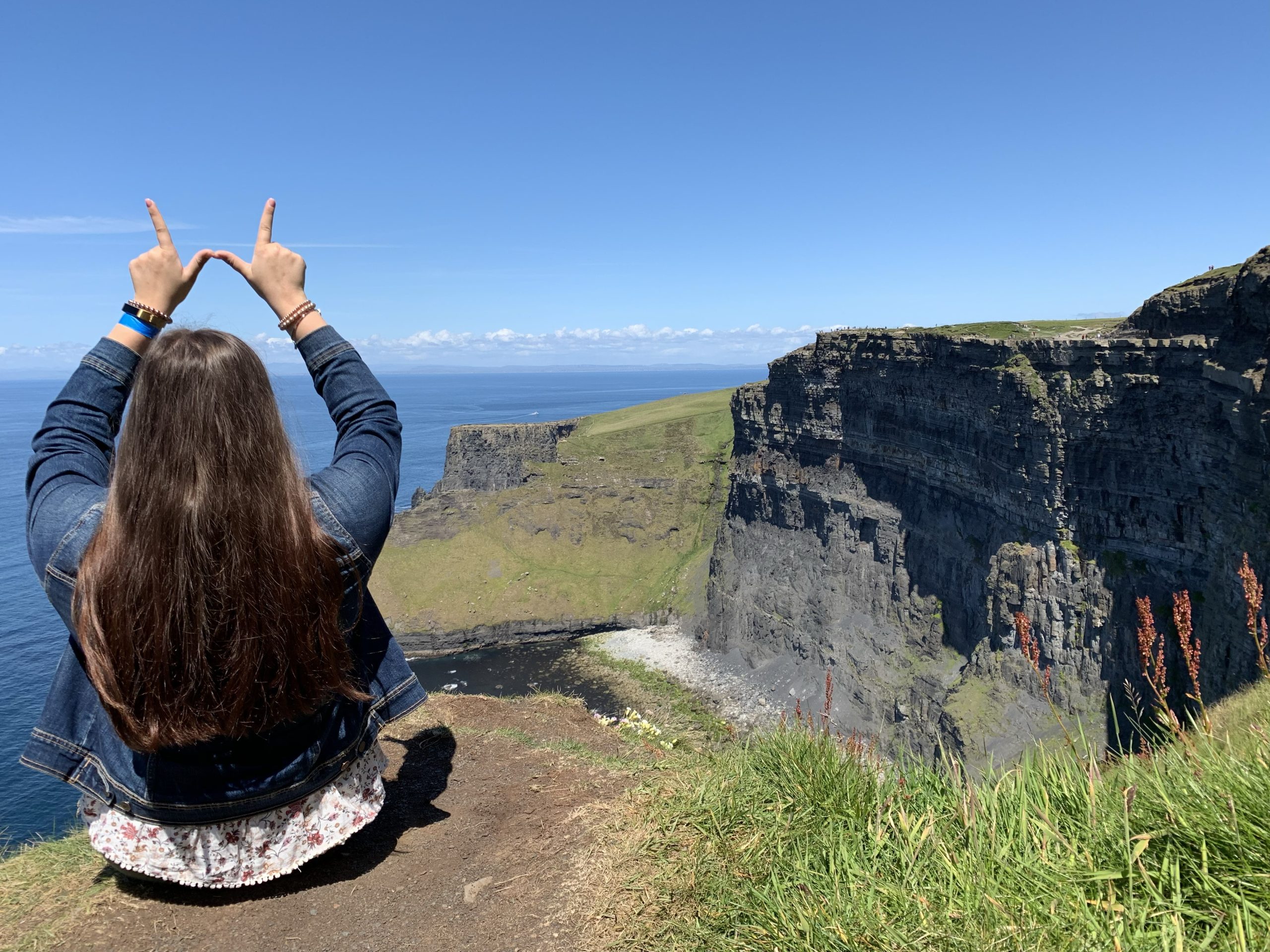 A UW nursing student sits on cliffs overlooking the sea during the Irish immersion program. Her back is to the camera and sheu0027s making the W hand sign.