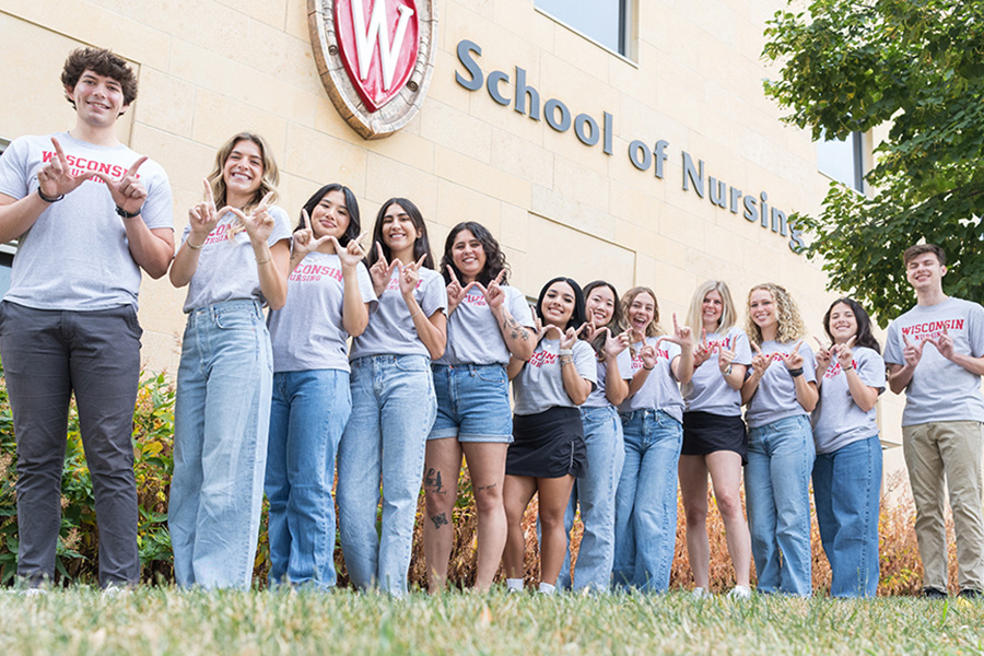 The 2024-25 UW–Madison School of Nursing Student Ambassadors stand in front of Signe Skott Cooper Hall making the W hand sign.