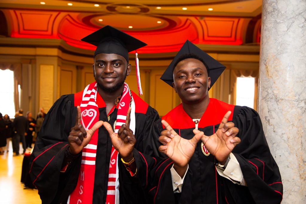 Famara Sanneh and a classmate in their caps and gowns on graduation day, making the W hand sign.