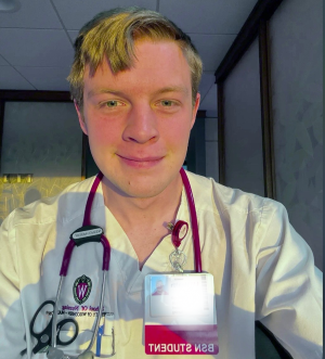 Green doing his clinicals in white coat, stethoscope, and BSN Student badge.