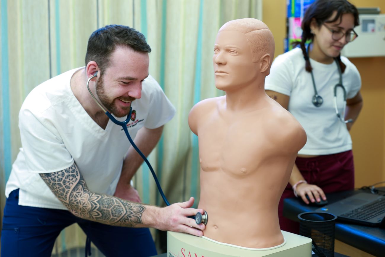 An ABSN student examines a medical mannequin with a stethoscope during a skills lab.