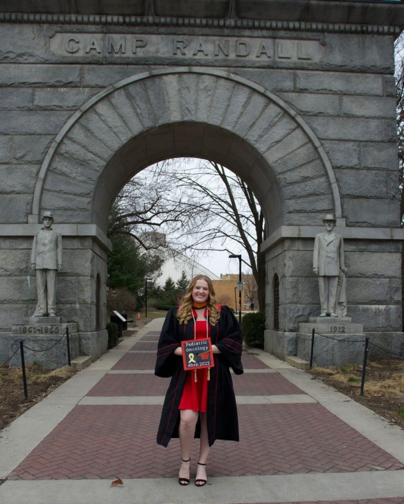 Debot at graduation standing under the iconic Memorial Arch at Camp Randall.