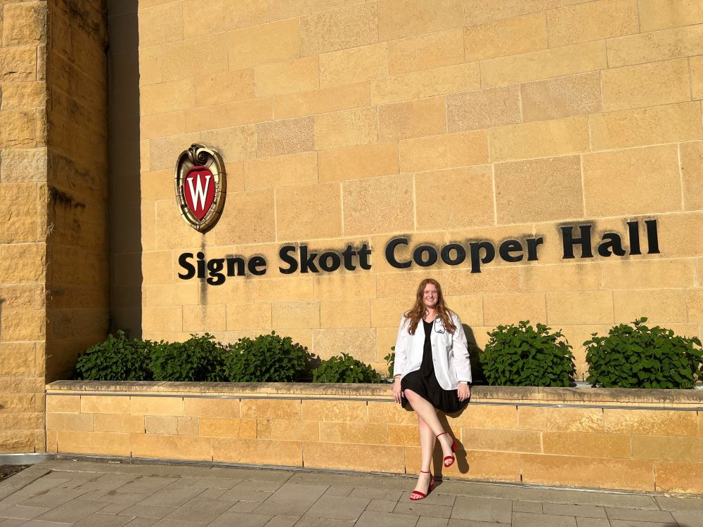 Debot in her white coat, sitting on the stone bench outside of Signe Skott Cooper Hall.