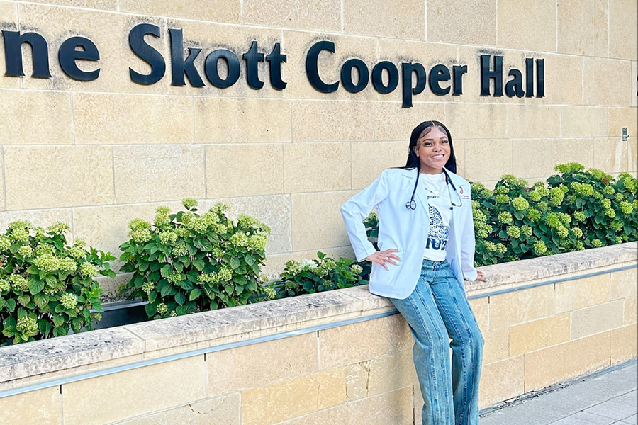 Diamond Wimbley, wearing her white coat, sits in front of Signe Skott Cooper Hall.