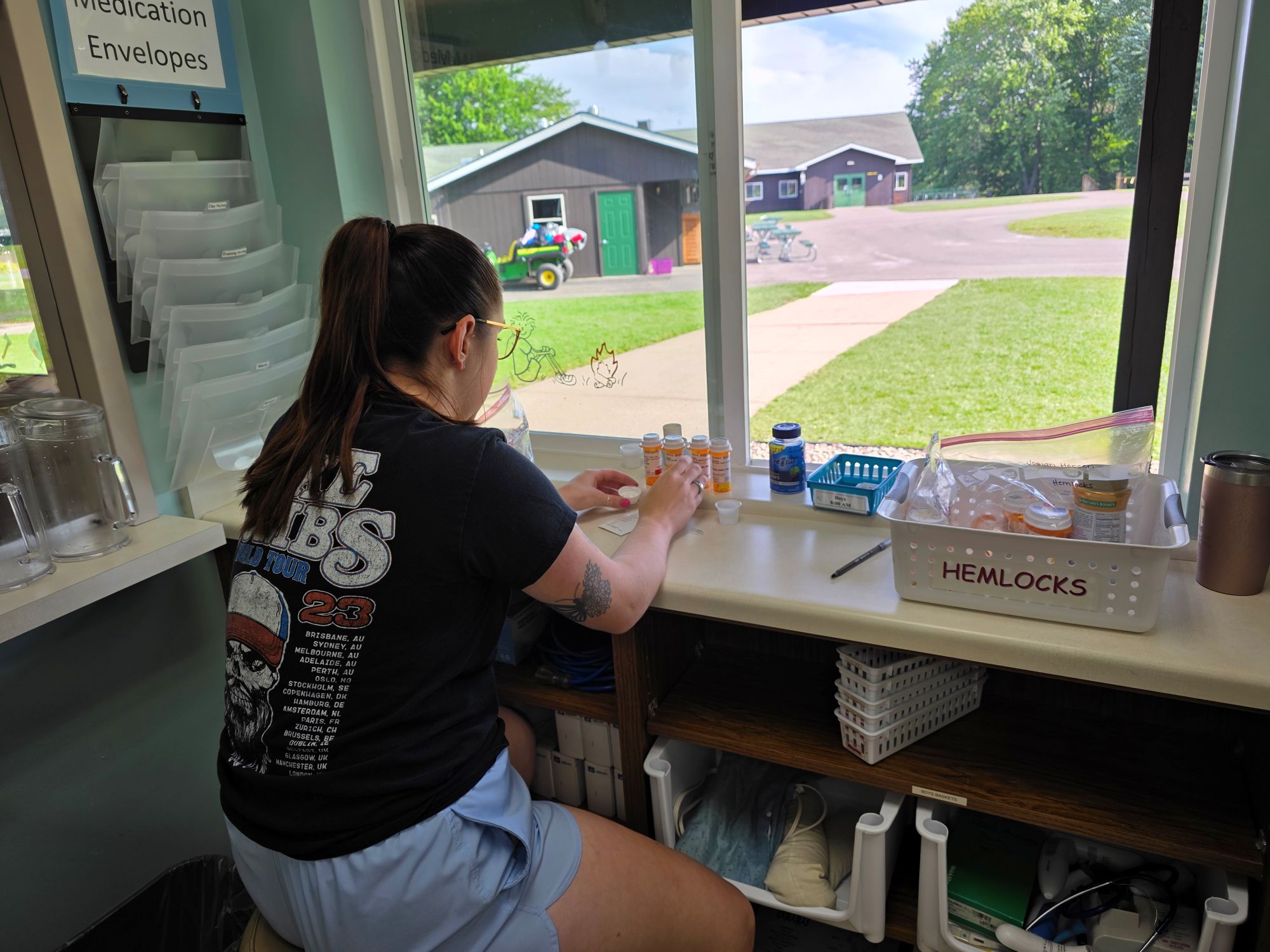 A camp counselor wearing shorts and a t-shirt gets medication for campers.