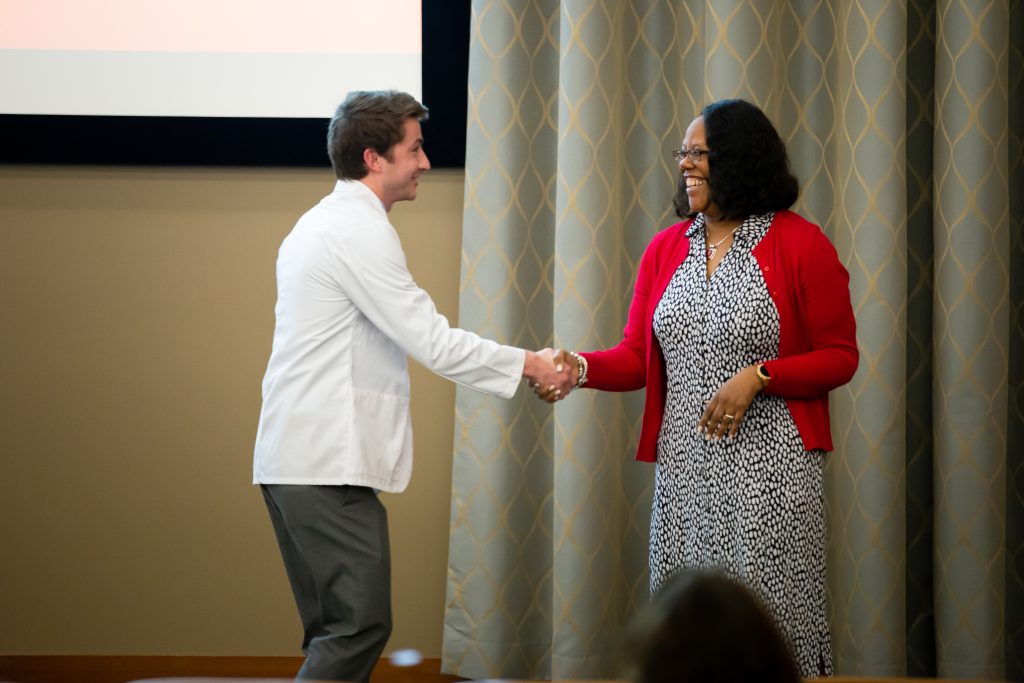 Linda D. Scott smiles and shakes the hand of a student on stage during the ABSN white coat ceremony.