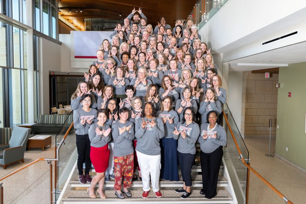 Dean Scott stands surrounded by School of Nursing faculty and staff on the staircase at Cooper Hall. They're all wearing gray