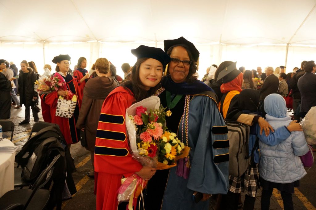 Dean Emerit Scott and a student lean against each other and smile during graduation.
