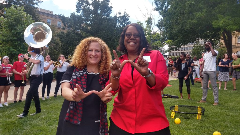 Linda D. Scott and Chancellor Jennifer Mnookin make the W hand sign in front of the UW marching band.