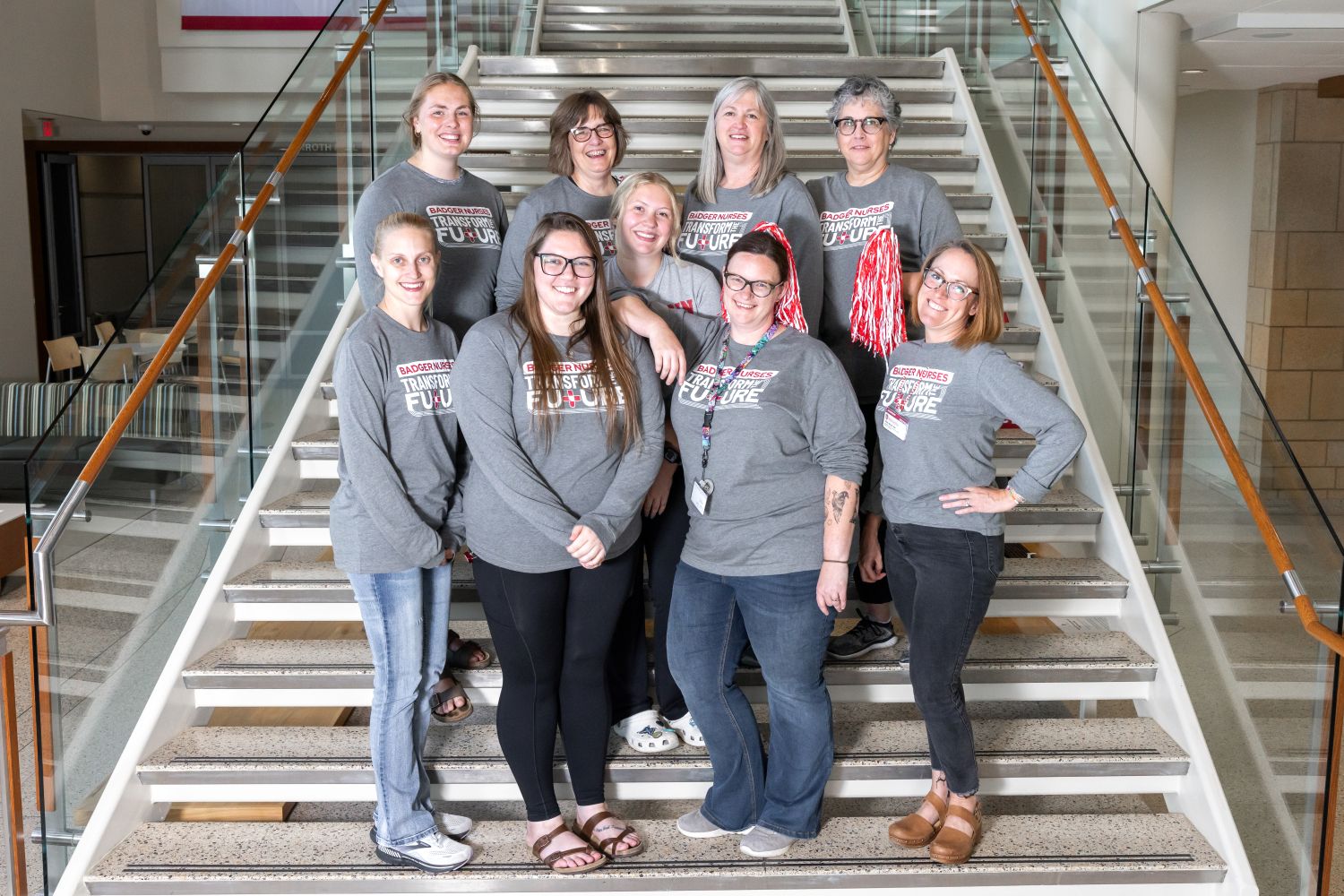 Rikki and the advising, admissions, and student services team poses on the stairs of Cooper Hall, wearing their gray "Badger Nurses Transform the Future" tshirts.