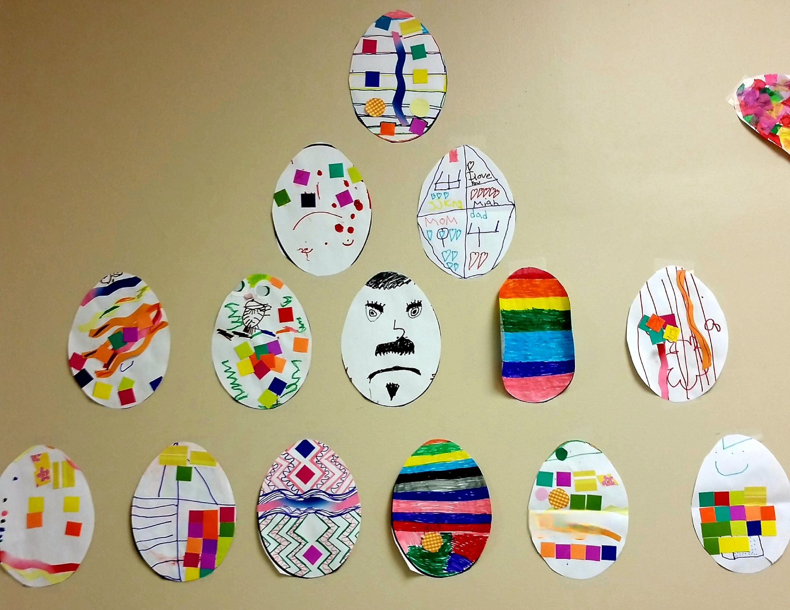 Brightly colored drawings of eggs hang on a wall. 
