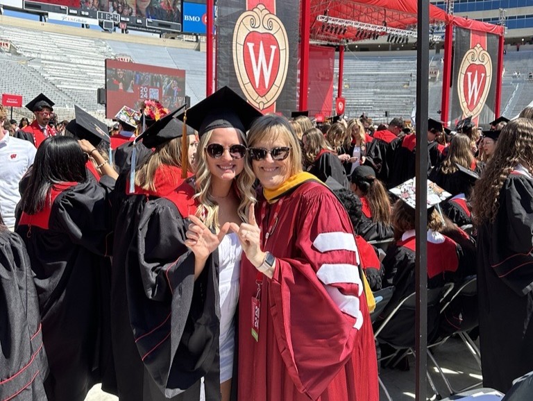 Judy Christensen and a graduating nursing student make the W hand sign at Camp Randall Stadium during graduation.