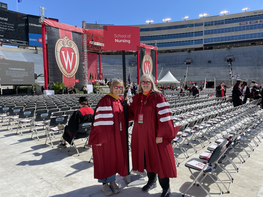 Judy Christensen and fellow admissions and recruitment team member Ann Larget pose in red robes at Camp Randall Stadium during graduation.
