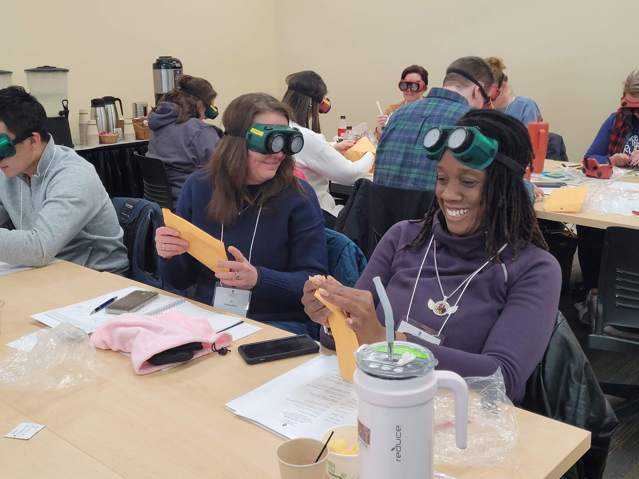 Participants in a CARE U Train the Trainer event laugh with each other as they wear goggles that simulate impaired senses.