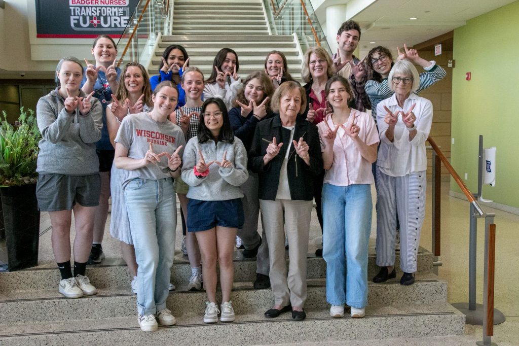 Students and their Badger Nursing alumni mentors pose on the stairway in Cooper Hall while making the W hand sign.