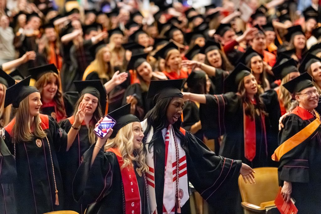 Deaton hugs a fellow BSN student at graduation on May 9, 2026 at the Kohl Center, as a sea of students in caps and gowns stand behind them.