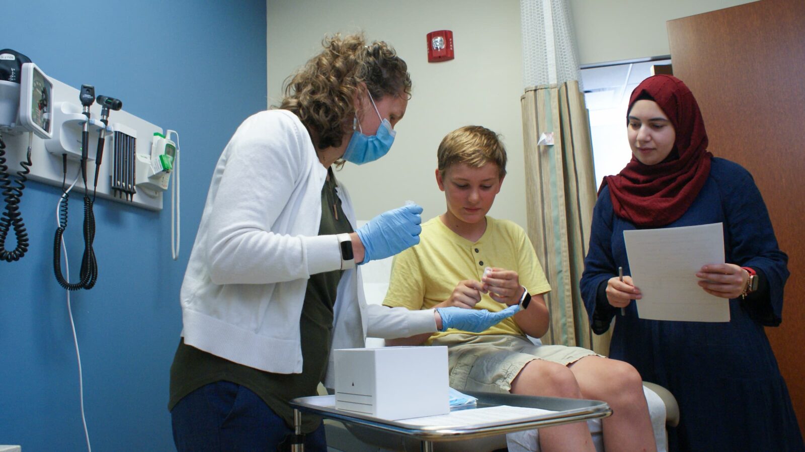 A PhD student and faculty member talk to a young patient and subject of their research study.