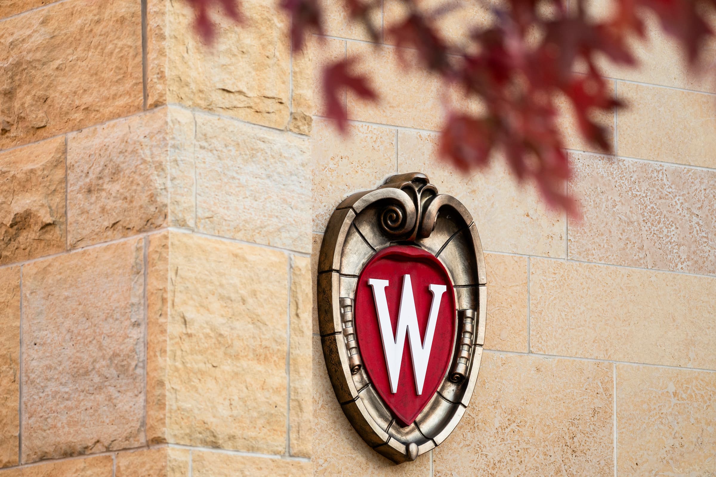 The UW crest on the outside of Signe Skott Cooper Hall is framed with red foliage on an autumn day at the University of Wisconsin–Madison on Oct. 29, 2025. (Photo by Taylor Wolfram / UW–Madison)